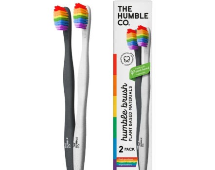 twee veganistische tandenborstels, één met een grijs handvat, één met een wit handvat, beide met regenboogkleurige nylon borstelharen naast een wit doosje met een afbeelding van beide tandenborstels erop